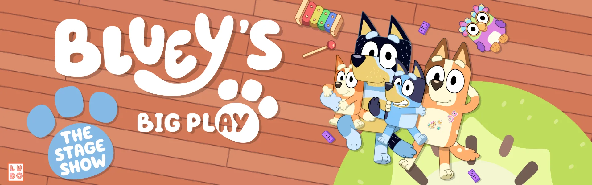 Promotional image for 'Bluey's Big Play: The Stage Show,' featuring the animated characters Bluey, Bingo, Bandit, and Chilli Heeler sitting on a wooden floor with toys scattered around.