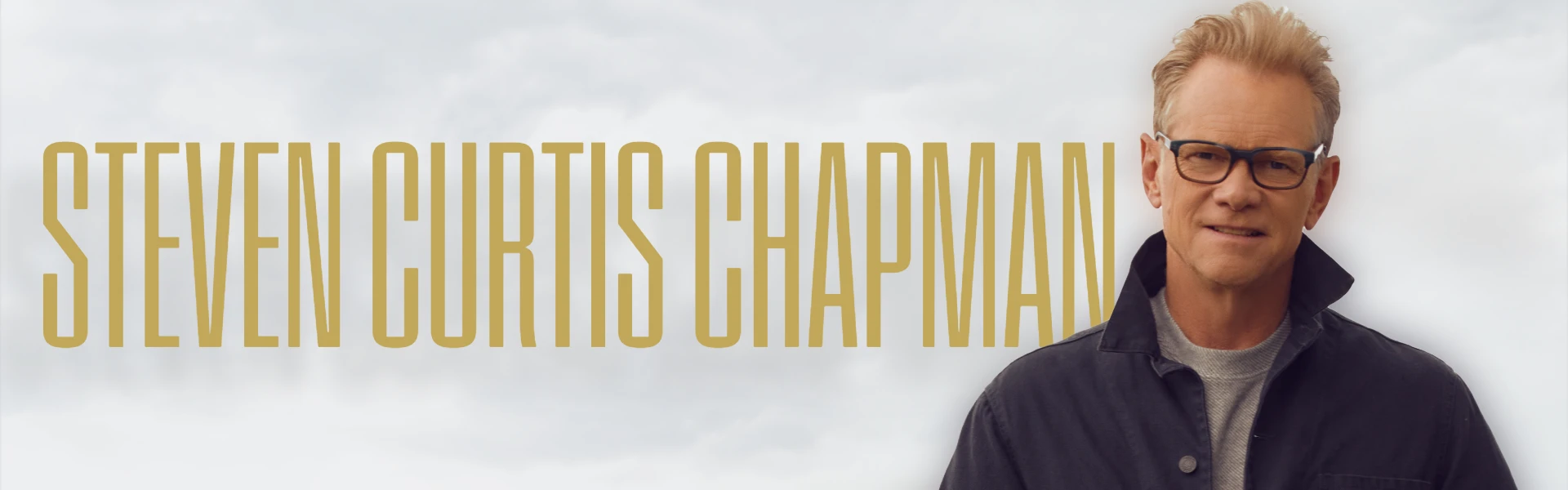 Promotional image for Steven Curtis Chapman, featuring the musician smiling and wearing glasses with his name in large gold letters against a cloudy sky background.