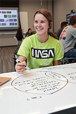Female student in class taking notes and smiling