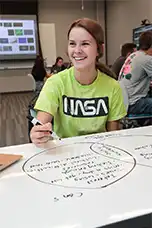 Female student in class taking notes and smiling