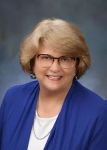 Woman with glasses in a blue top, wearing a necklace and earrings. (Mary Wendt)