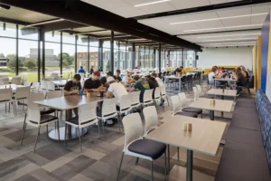 Spacious college cafeteria with large windows and students sitting at tables.