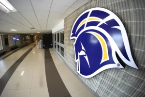 Hallway inside the NIACC gymnasium with a large blue and gold Trojan head logo on the wall.