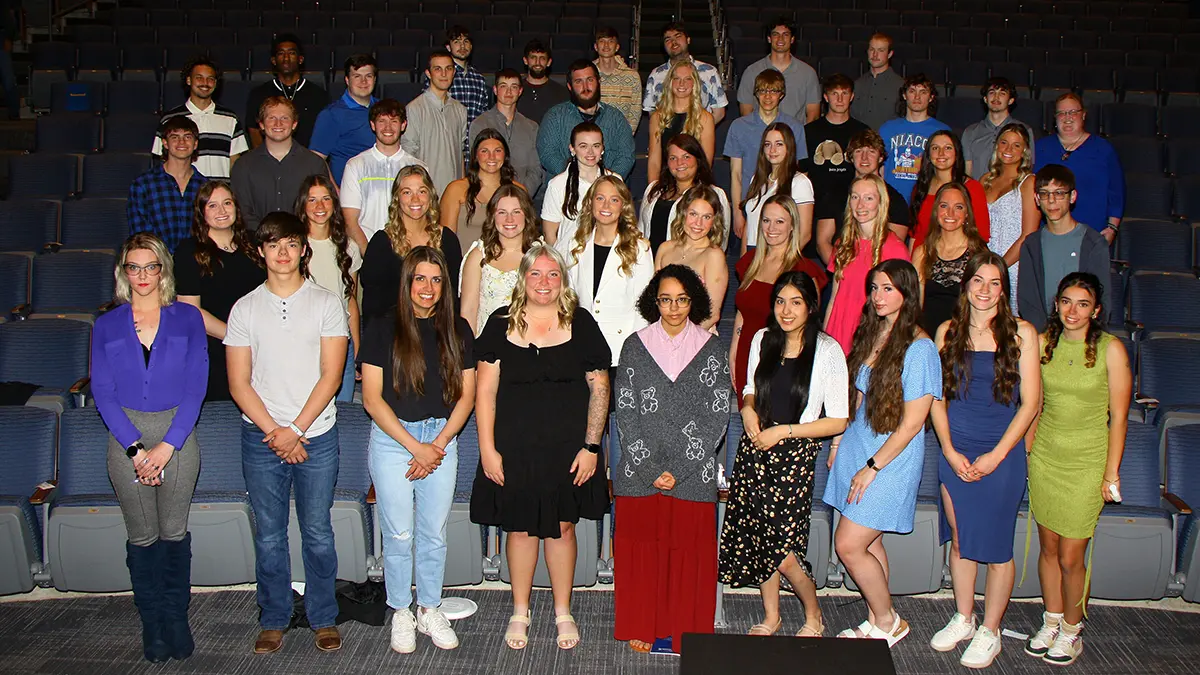 Large group of students posing together in an auditorium, standing in rows for a group photo.