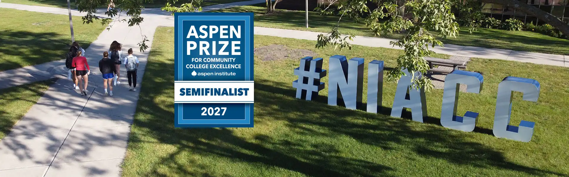 Students walk along a campus path near large NIACC letters, alongside a graphic announcing NIACC as a 2027 Aspen Prize for Community College Excellence semifinalist.