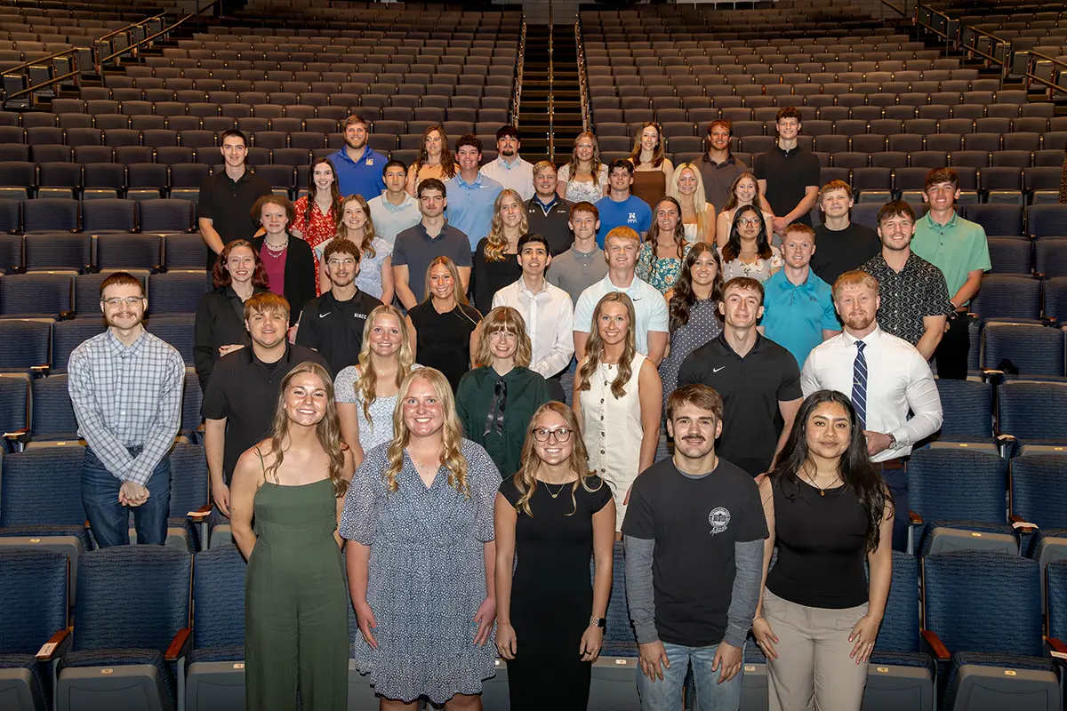 Large group of students posing together in an auditorium for a group photo, standing in rows among theater seats.