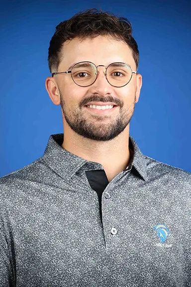 Smiling man with short dark hair, a beard, and round glasses wearing a gray polo shirt against a blue background.