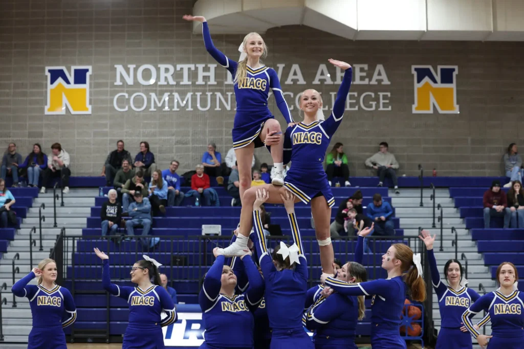 NIACC cheerleaders perform a stunt during a campus event, with two cheerleaders elevated above their teammates in the gymnasium.