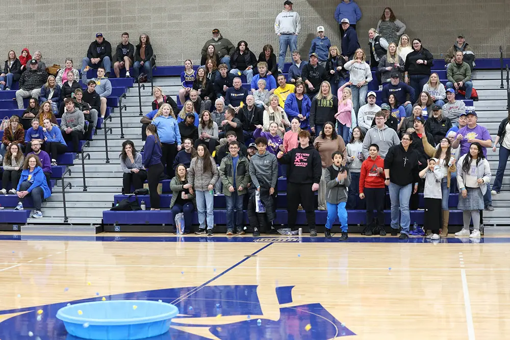A large crowd of students and community members stands in the NIACC gymnasium bleachers during a campus event.